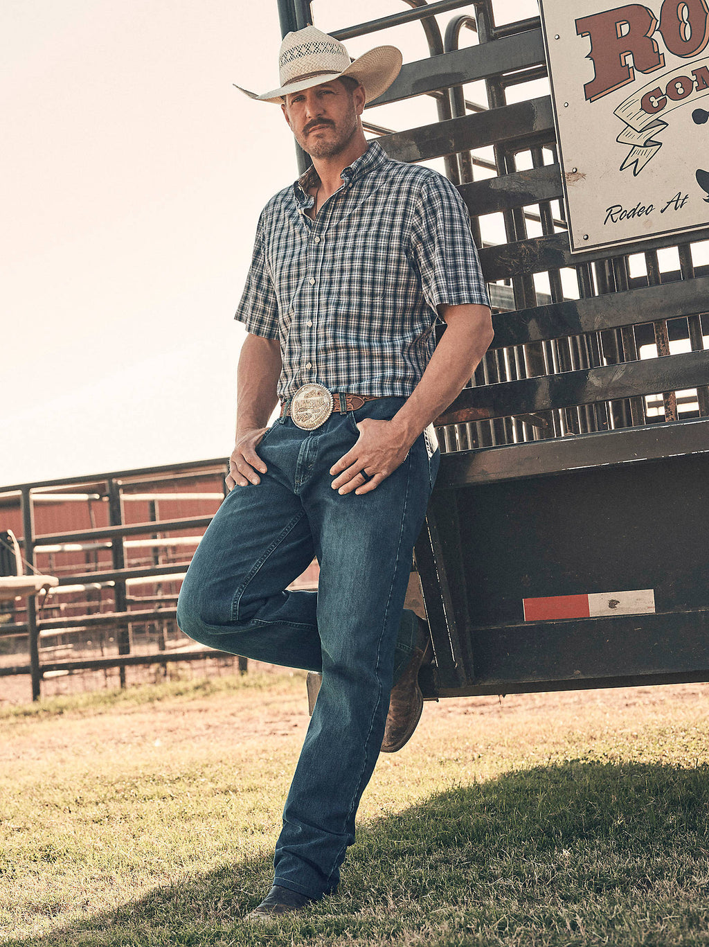 Wrangler Men's 20X No. 01 Relaxed Fit Jeans in River Wash, outdoor view at a rodeo fence