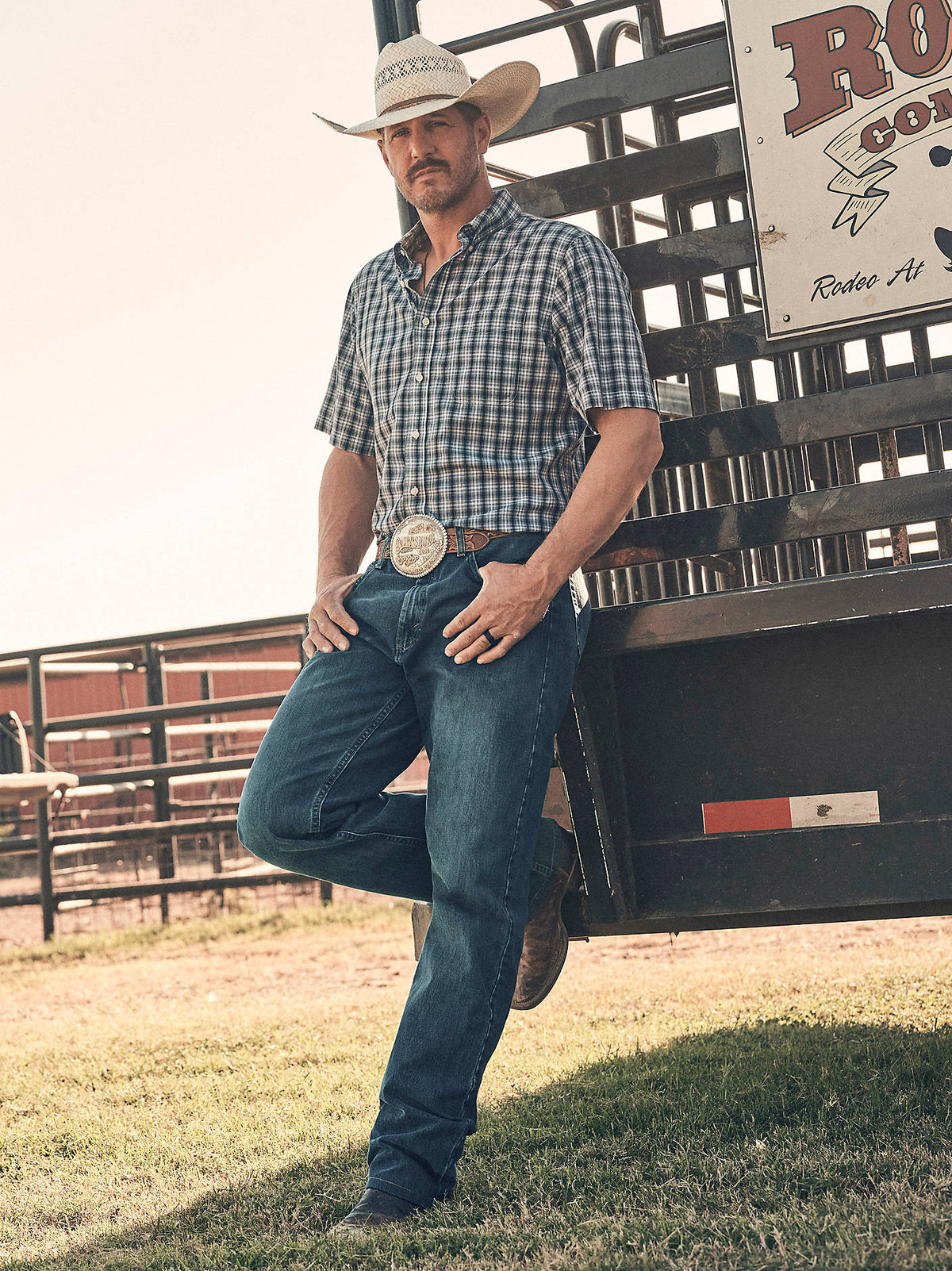 Wrangler Men's 20X No. 01 Relaxed Fit Jeans in River Wash, outdoor view at a rodeo fence