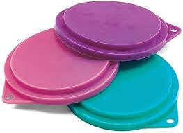 Three vibrant, circular silicone pet food can covers in purple, pink, and teal.