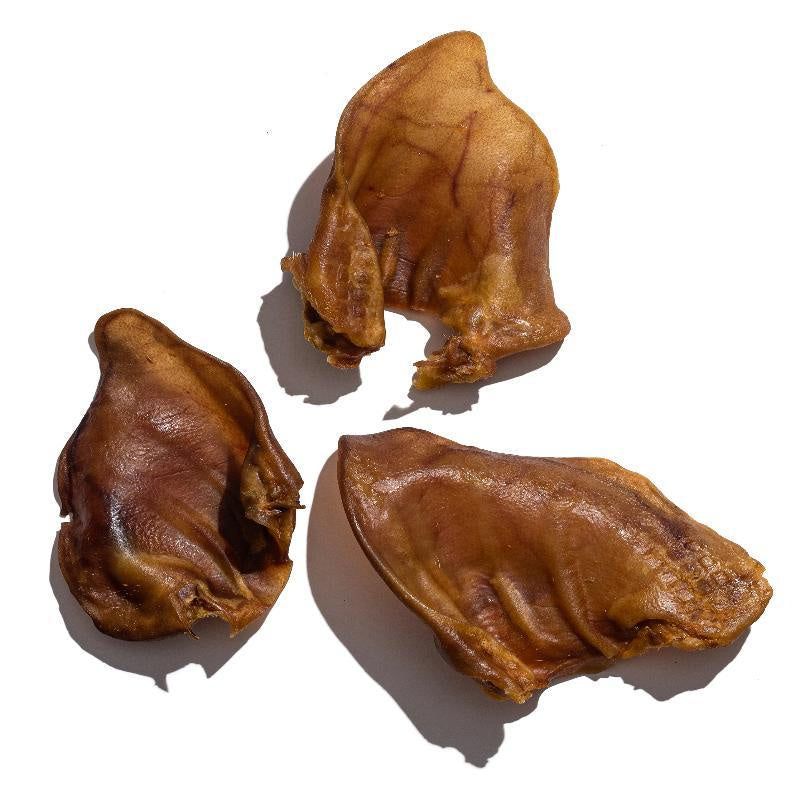 Three dried pig ear dog treats arranged on a white background.