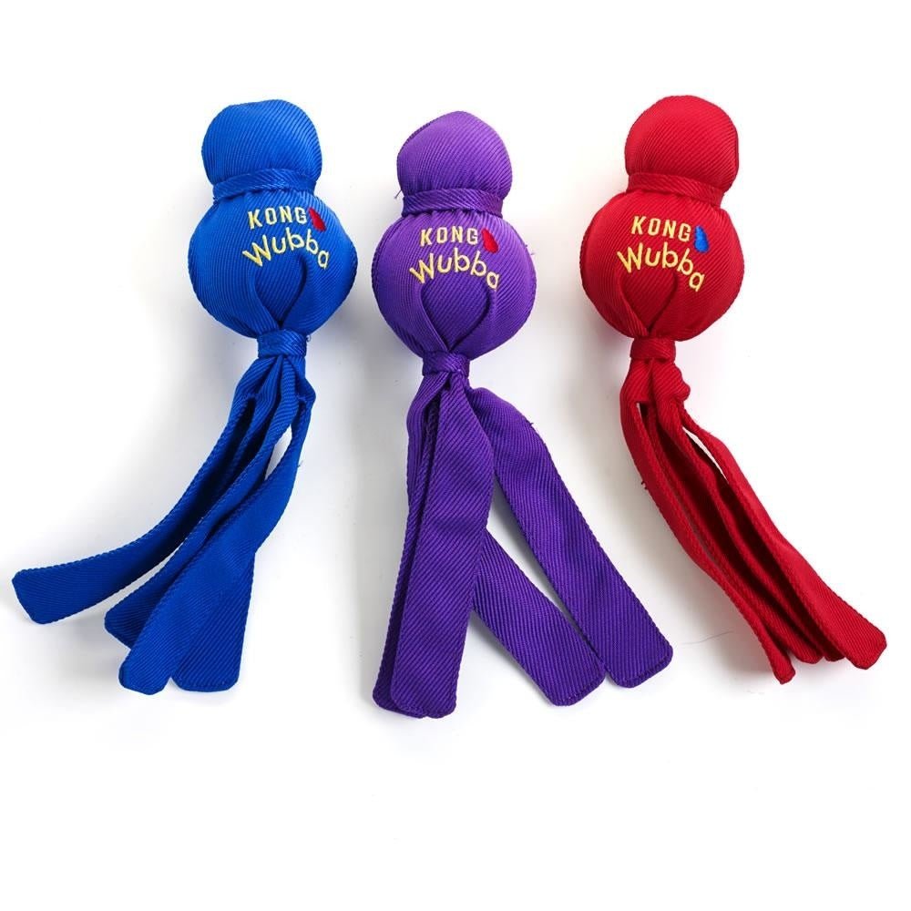 Three Kong Wubba dog toys in blue, purple, and red, each featuring two balls and long fabric tails.