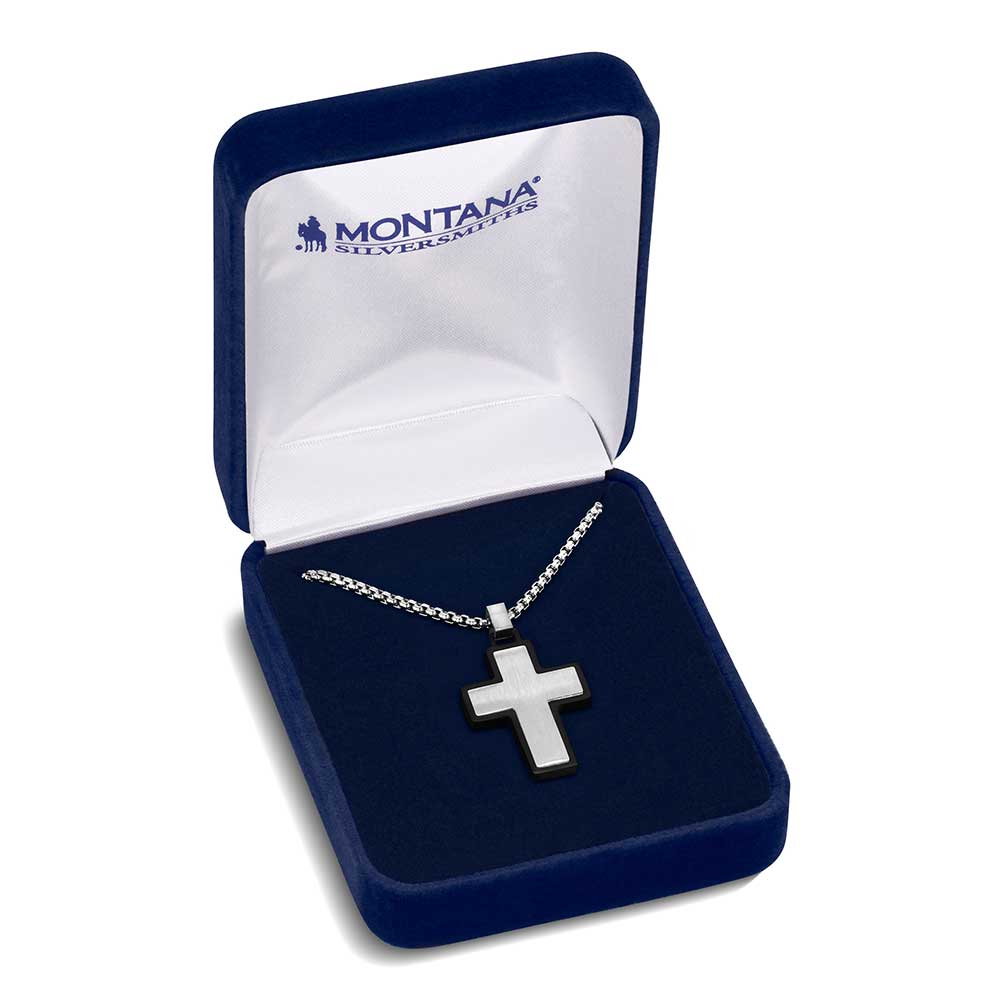 A silver and black nickel cross pendant hangs from a chain inside a blue velvet jewelry box.