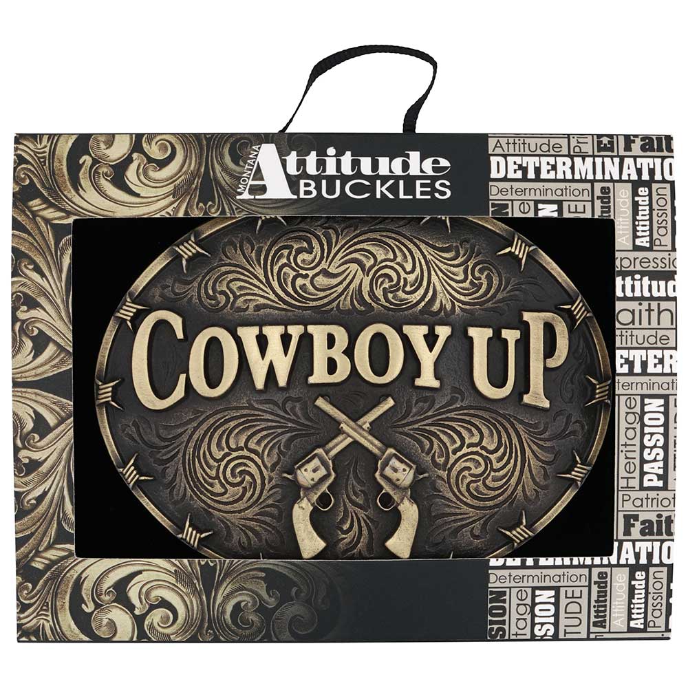 An oval Montana Silversmiths belt buckle featuring the words Cowboy Up and two crossed revolvers.