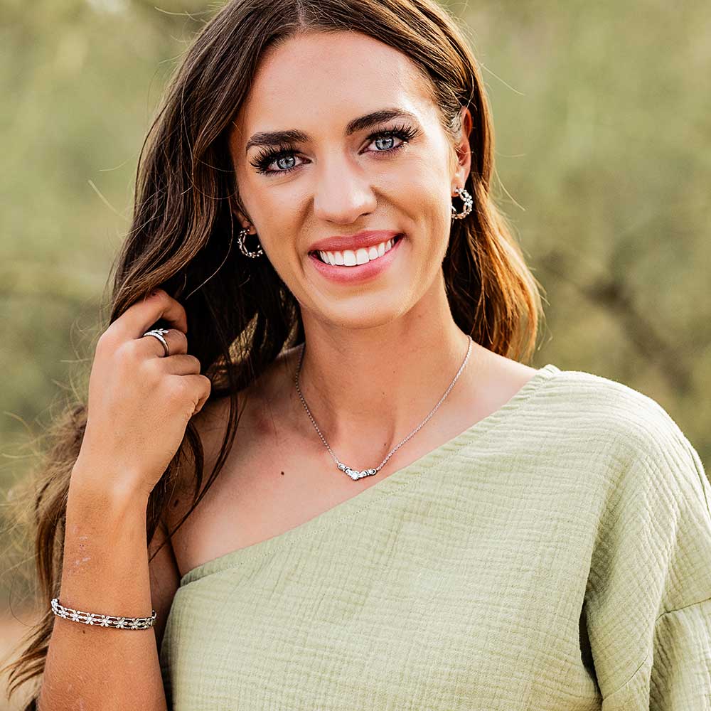 A woman wears silver hoop earrings featuring a floral design with clear cubic zirconia centers.