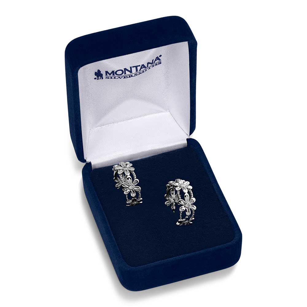 A pair of silver-tone floral hoop earrings with cubic zirconia centers inside a blue velvet box.