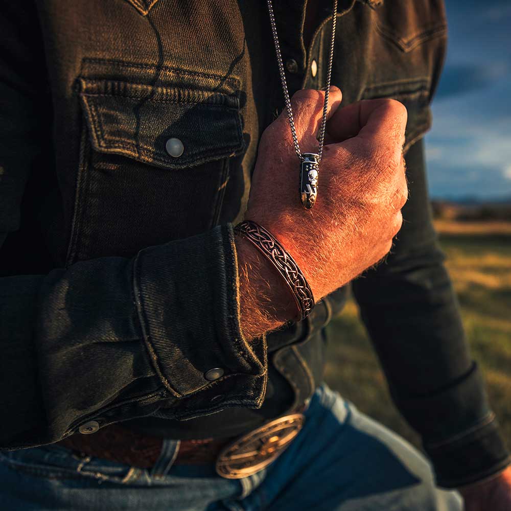 A silver bullet pendant with a skull design and rose gold tip hangs on a chain around a man's neck.