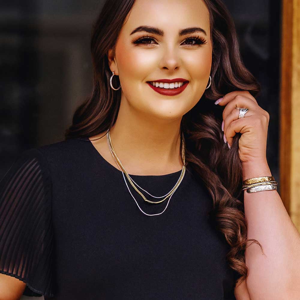 A woman wears a three-strand layered necklace featuring silver and gold-toned chains.