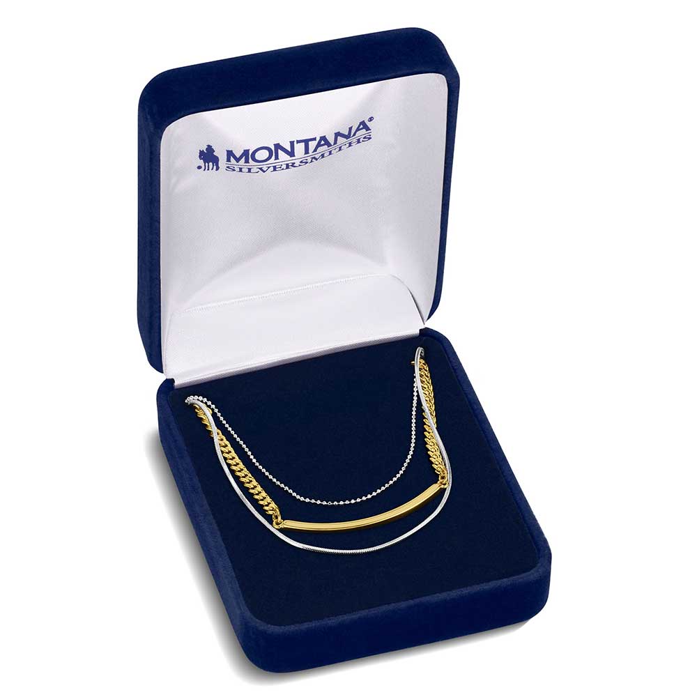 A layered necklace with silver and gold tone chains displayed in a blue velvet jewelry box.