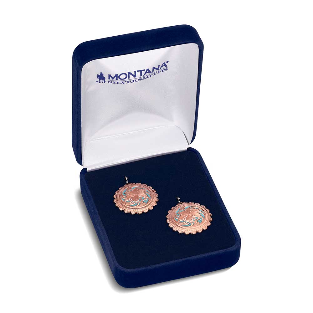 A pair of round rose gold earrings with turquoise floral centers inside a blue velvet gift box.