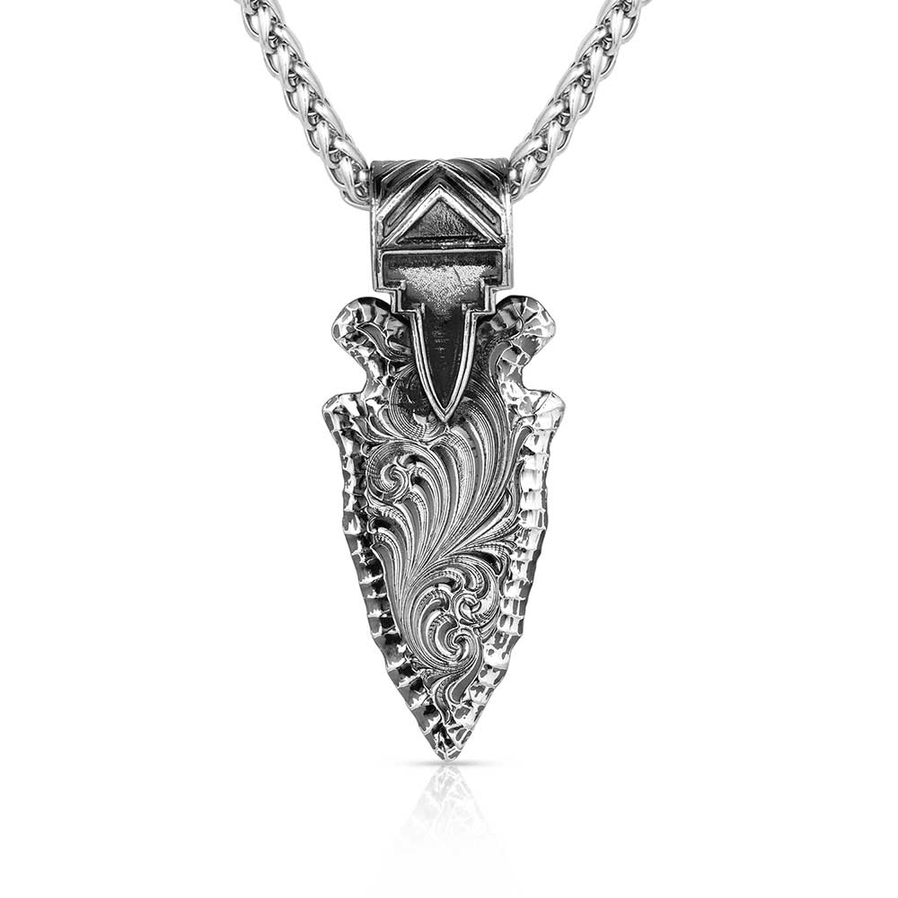 A gunmetal arrowhead pendant with intricate Western engraving hangs from a silver wheat chain.