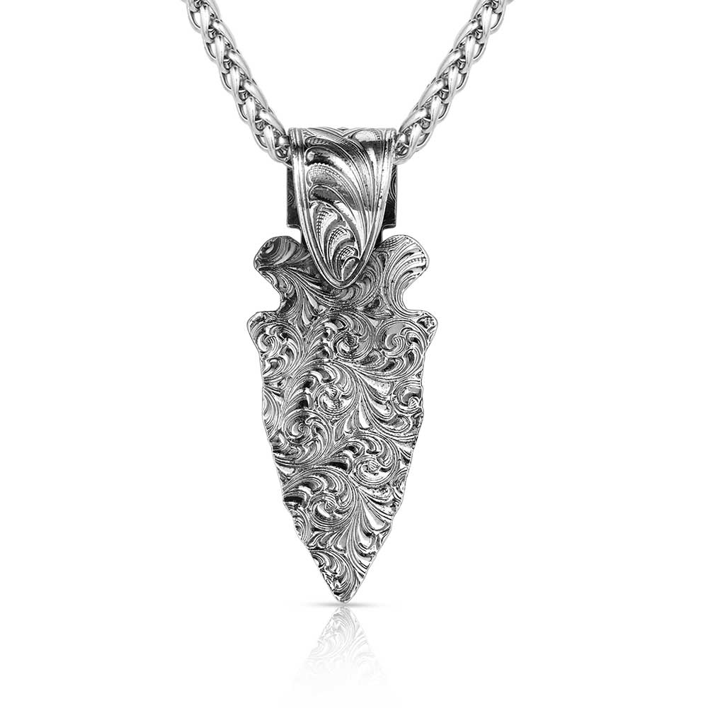 A gunmetal arrowhead pendant with intricate Western engraving hangs from a silver wheat chain.