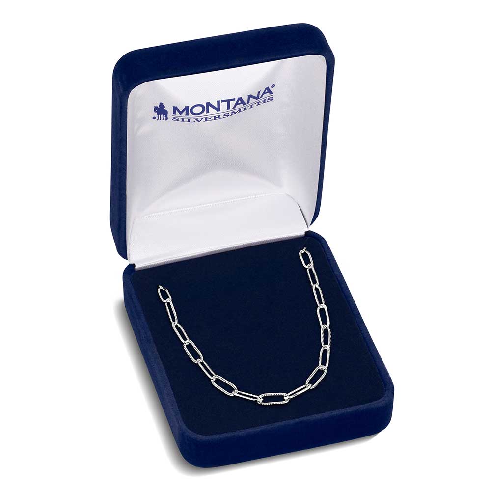 A silver paperclip chain necklace displayed inside an open blue velvet jewelry box.