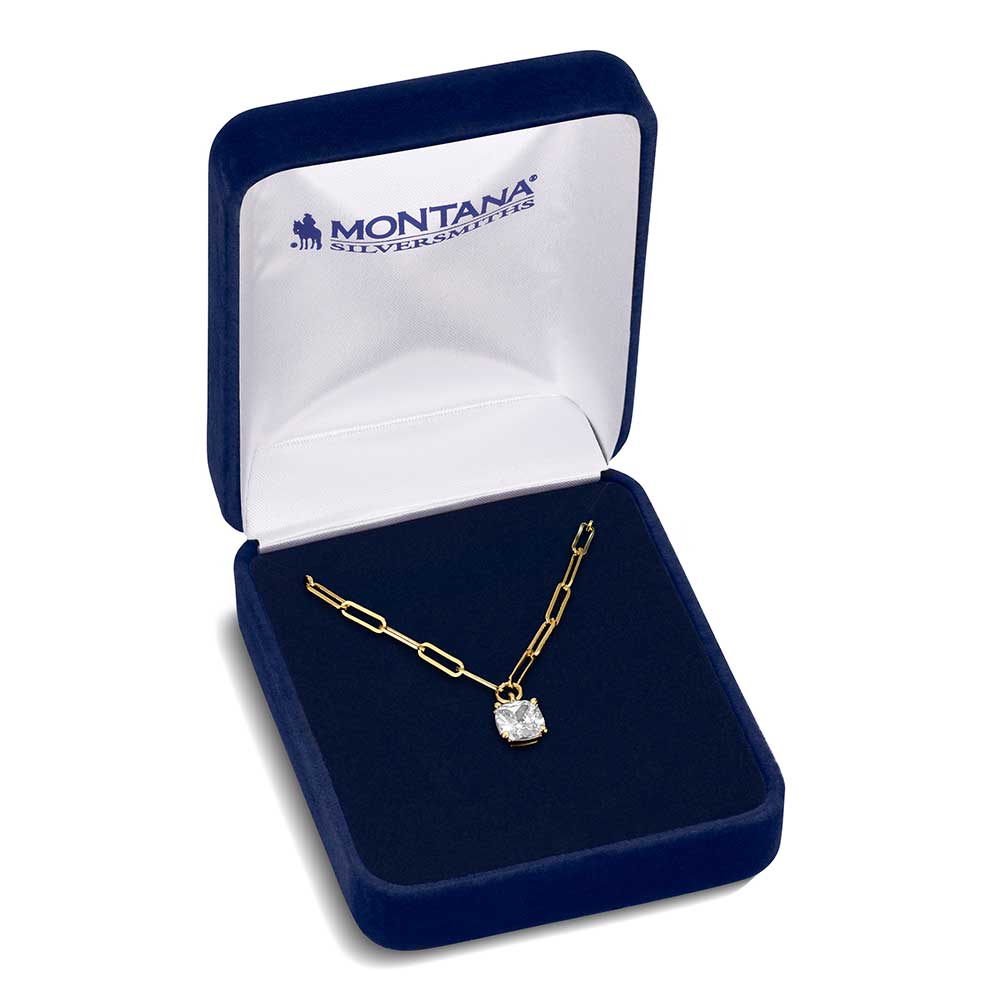 A gold tone paperclip chain necklace with a solitaire crystal pendant inside a blue velvet box.