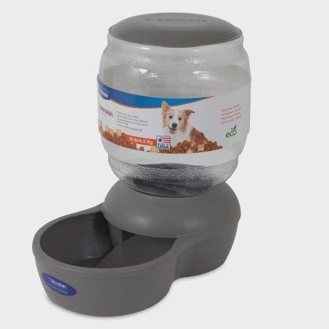 A gray gravity-fed pet food dispenser with a clear plastic storage bottle on a base.
