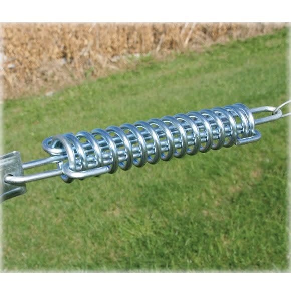 A silver metal tension spring is shown horizontally against a blurred grassy background.